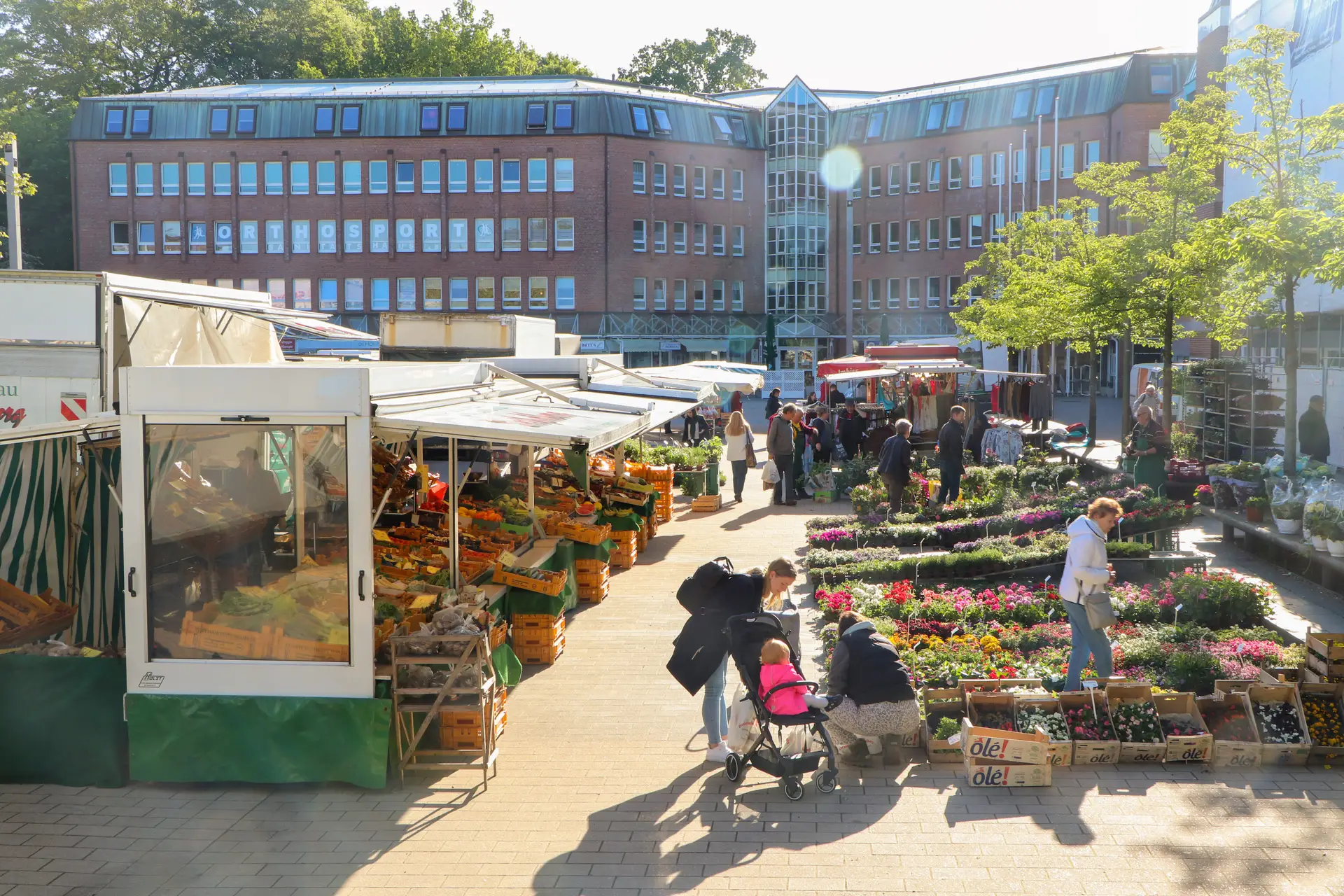 Wochenmarkt am Morgen im Frühling: Stände und Marktstände mit Verkaufswaren vor dem Hintergrund von Passanten.