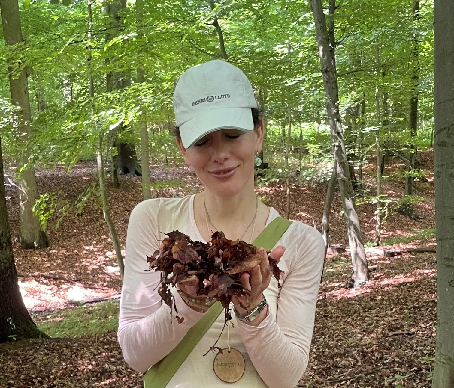 Eine Person mit Outdoor-Kleidung steht im Herbstwald; im Hintergrund sind Bäume mit buntem Laub und der Weg im Wald sichtbar.